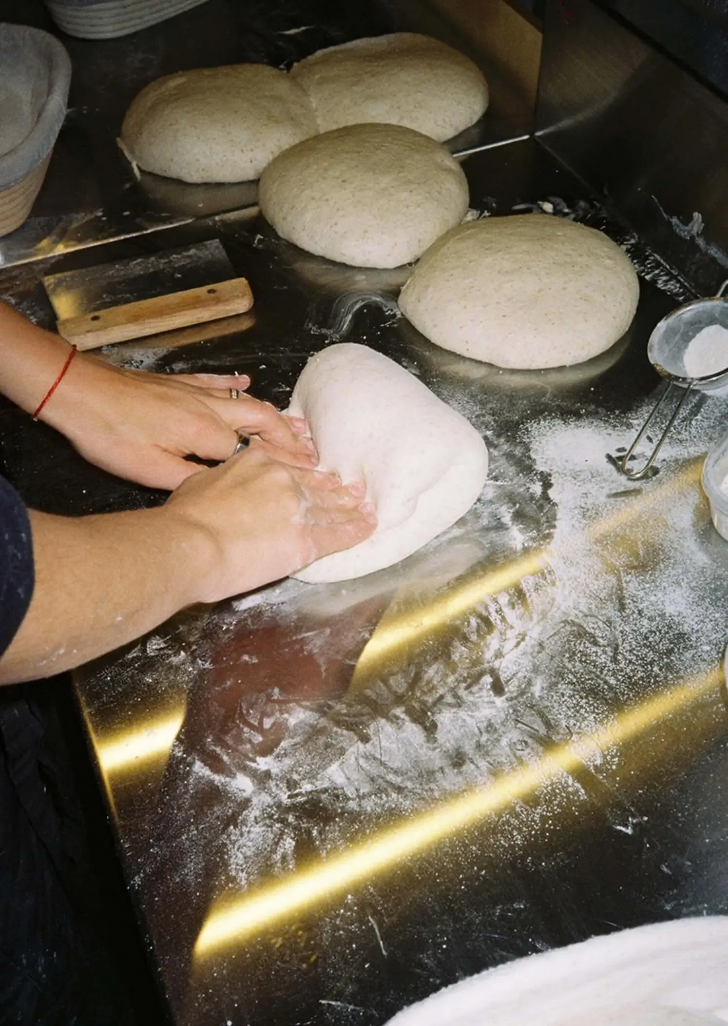 粉の広がる作業台でパン生地を成形する手